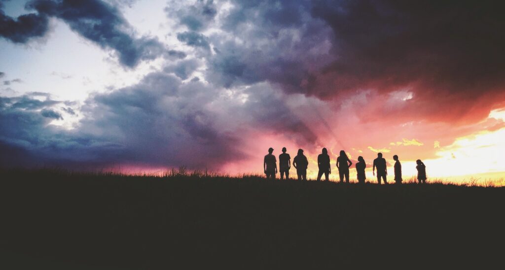 Silhouetted group of colleagues standing on a hilltop under a stormy sunset sky