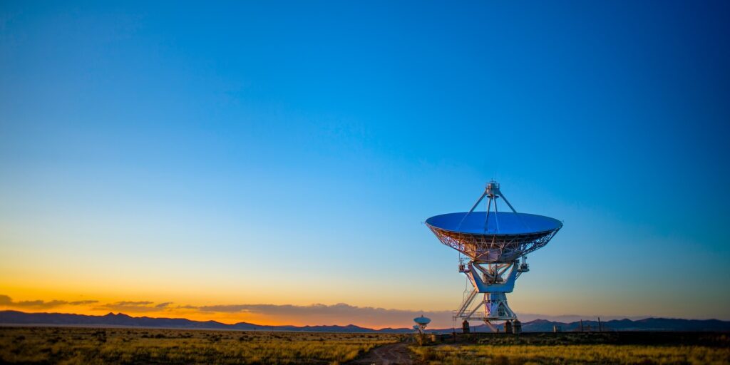 Radio telescope dish on open grassland at sunset